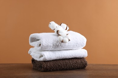 Photo of Stack of clean towels and cotton flowers on wooden table against brown background
