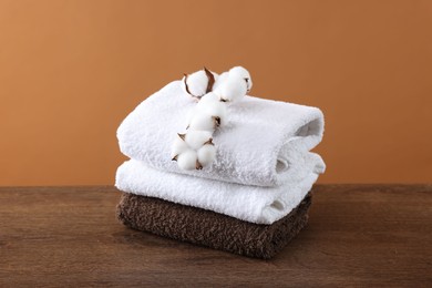 Photo of Stack of clean towels and cotton flowers on wooden table against brown background