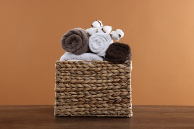 Photo of Clean towels and cotton flowers in basket on wooden table against brown background