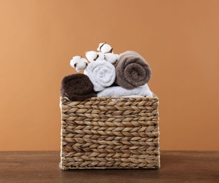 Photo of Clean towels and cotton flowers in basket on wooden table against brown background
