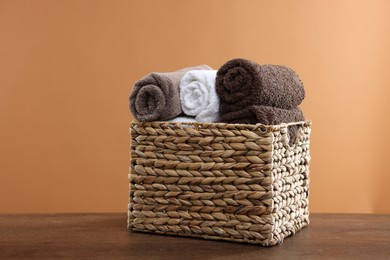 Photo of Clean towels in basket on wooden table against brown background