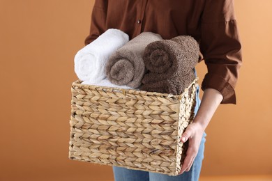 Photo of Woman holding basket with clean towels on brown background, closeup