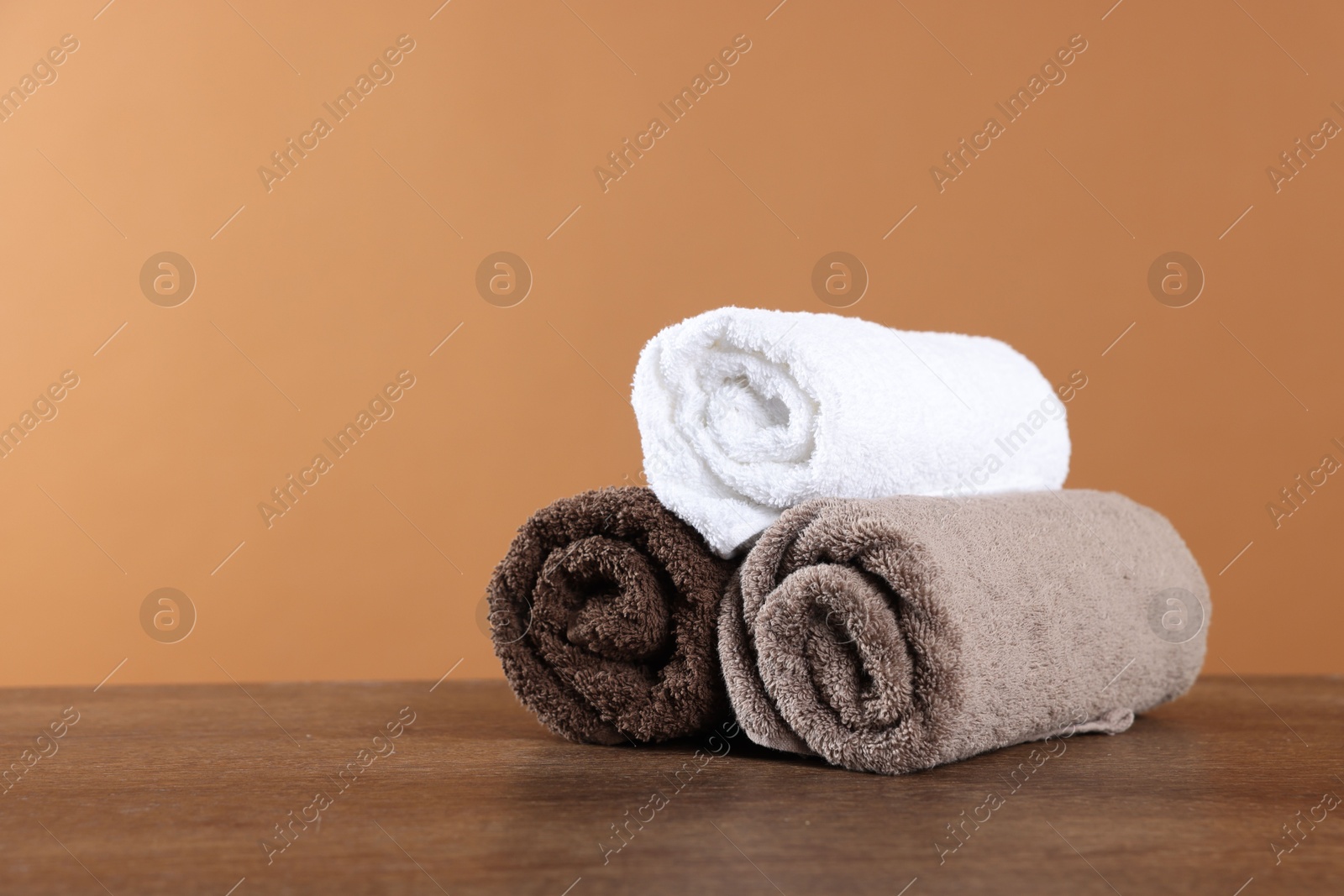 Clean terry towels on wooden table against brown background, space for text Photo of Clean terry towels on wooden table against brown background, space for text