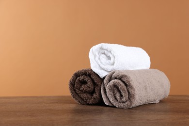 Photo of Clean terry towels on wooden table against brown background, space for text