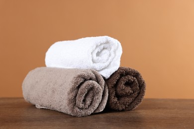 Photo of Clean terry towels on wooden table against brown background