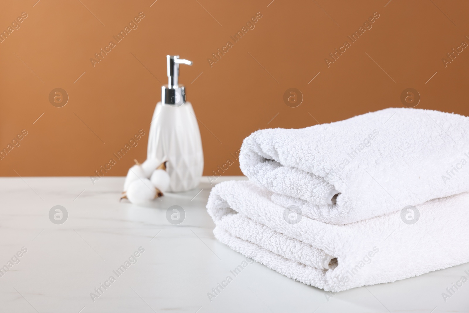 Clean terry towels, cosmetic product and cotton flower on light table against brown background Photo of Clean terry towels, cosmetic product and cotton flower on light table against brown background