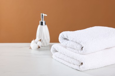 Photo of Clean terry towels, cosmetic product and cotton flower on light table against brown background