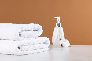 Photo of Clean terry towels, cosmetic product and cotton flower on light table against brown background