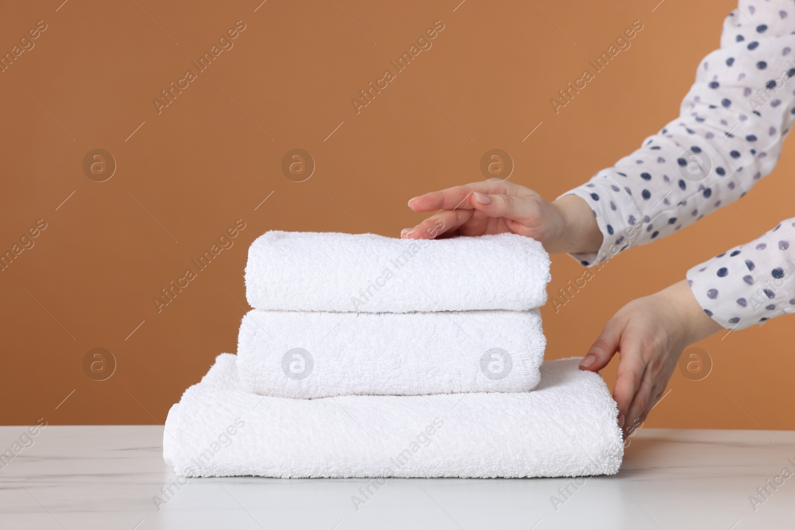 Woman stacking clean towels at white marble table against brown background, closeup Photo of Woman stacking clean towels at white marble table against brown background, closeup