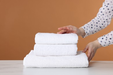 Photo of Woman stacking clean towels at white marble table against brown background, closeup