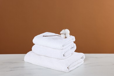 Photo of Clean terry towels and cotton flower on white marble table against brown background