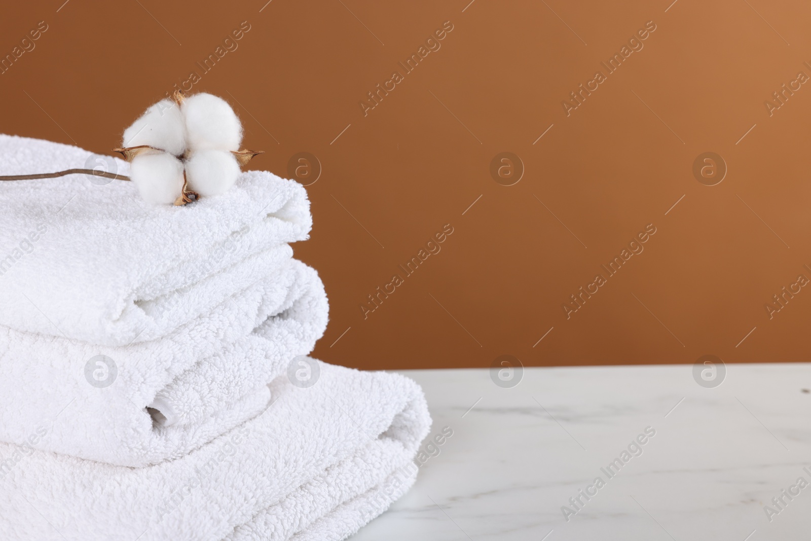 Clean terry towels and cotton flower on white marble table against brown background, closeup. Space for text Photo of Clean terry towels and cotton flower on white marble table against brown background, closeup. Space for text