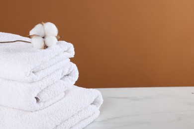 Photo of Clean terry towels and cotton flower on white marble table against brown background, closeup. Space for text