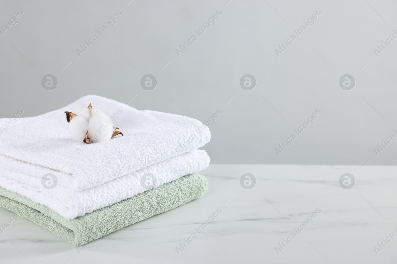 Clean terry towels and cotton flower on white marble table against light background, space for text Photo of Clean terry towels and cotton flower on white marble table against light background, space for text