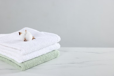 Photo of Clean terry towels and cotton flower on white marble table against light background, space for text