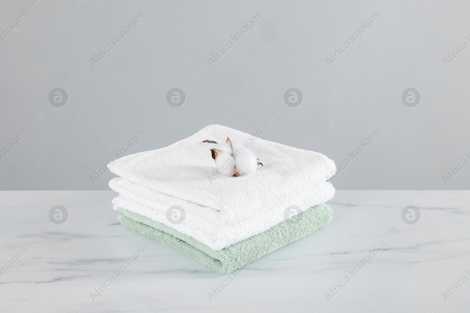 Clean terry towels and cotton flower on white marble table against light background Photo of Clean terry towels and cotton flower on white marble table against light background