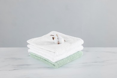 Photo of Clean terry towels and cotton flower on white marble table against light background