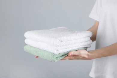 Photo of Woman holding stack of clean towels on light background, closeup