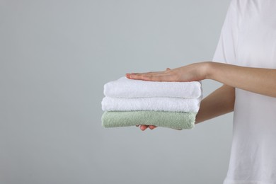 Photo of Woman holding stack of clean towels on light background, closeup. Space for text