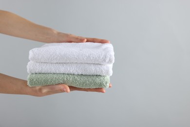 Photo of Woman holding stack of clean towels on light background, closeup. Space for text