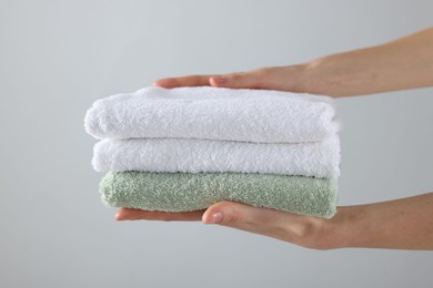 Photo of Woman holding stack of clean towels on light background, closeup