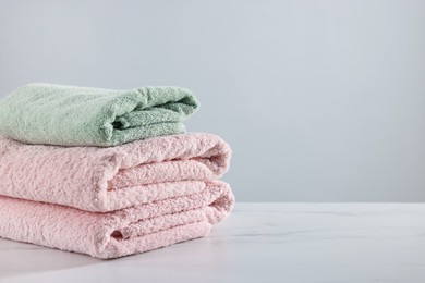 Photo of Stack of clean towels on white marble table against light background, space for text