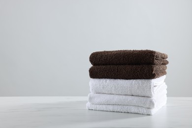 Photo of Stack of clean towels on white marble table against light background, space for text
