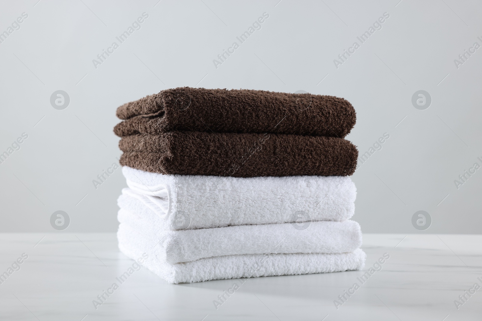 Stack of clean towels on white marble table against light background Photo of Stack of clean towels on white marble table against light background