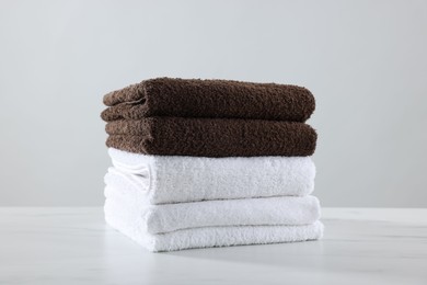 Photo of Stack of clean towels on white marble table against light background