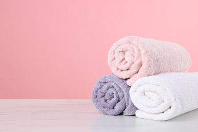 Photo of Clean towels on light marble table against pink background, space for text