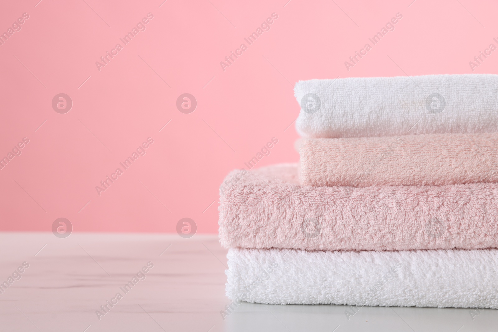 Stack of clean towels on light marble table against pink background, closeup. Space for text Photo of Stack of clean towels on light marble table against pink background, closeup. Space for text
