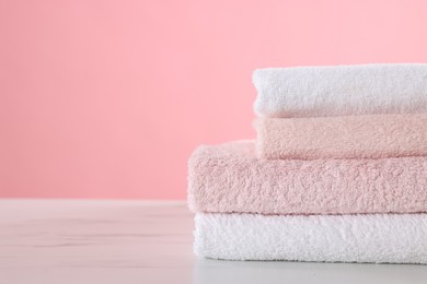 Photo of Stack of clean towels on light marble table against pink background, closeup. Space for text