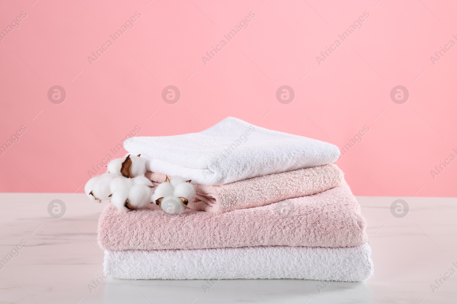 Stack of clean towels and cotton flowers on light marble table against pink background Photo of Stack of clean towels and cotton flowers on light marble table against pink background