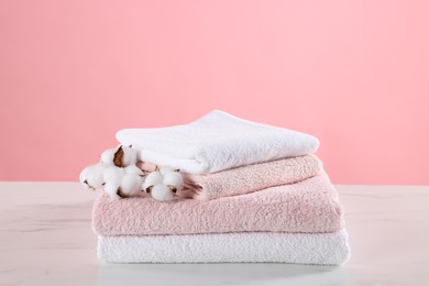 Photo of Stack of clean towels and cotton flowers on light marble table against pink background