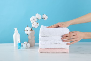 Photo of Woman stacking clean towels at white marble table against light blue background, closeup