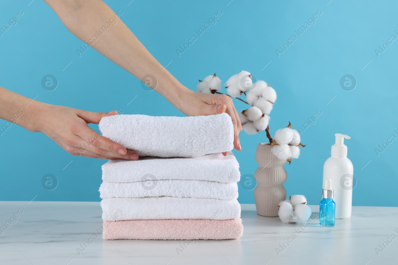 Woman stacking clean towels at white marble table against light blue background, closeup Photo of Woman stacking clean towels at white marble table against light blue background, closeup