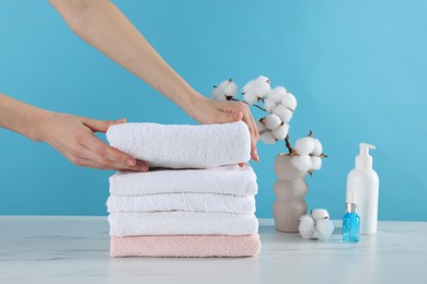 Photo of Woman stacking clean towels at white marble table against light blue background, closeup