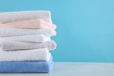 Photo of Stack of clean towels on white marble table against light blue background, closeup. Space for text