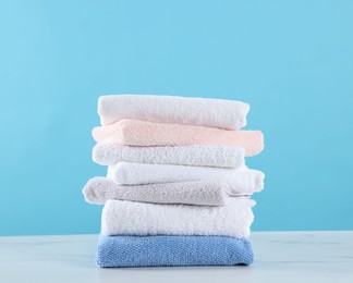 Photo of Stack of clean towels on white marble table against light blue background