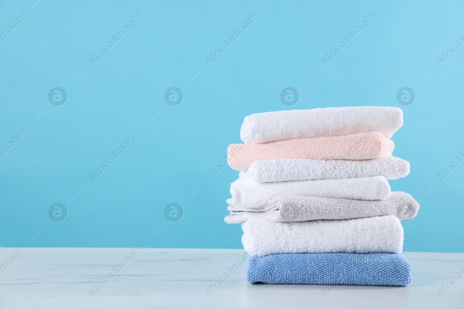 Stack of clean towels on white marble table against light blue background, space for text Photo of Stack of clean towels on white marble table against light blue background, space for text