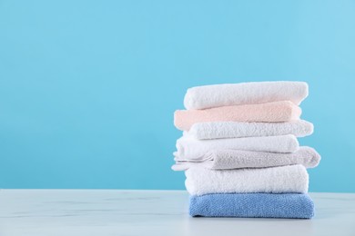 Photo of Stack of clean towels on white marble table against light blue background, space for text