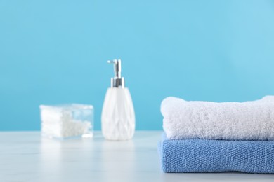 Photo of Clean towels, cosmetic product and cotton swabs on white marble table against light blue background