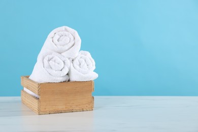 Photo of Clean towels in wooden box on white marble table against light blue background, space for text