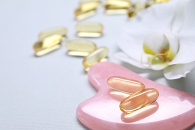 Photo of Collagen capsules, gua sha and flower on white background, closeup. Space for text