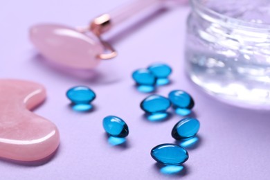 Photo of Collagen capsules, gel, face roller and gua sha on violet background, closeup