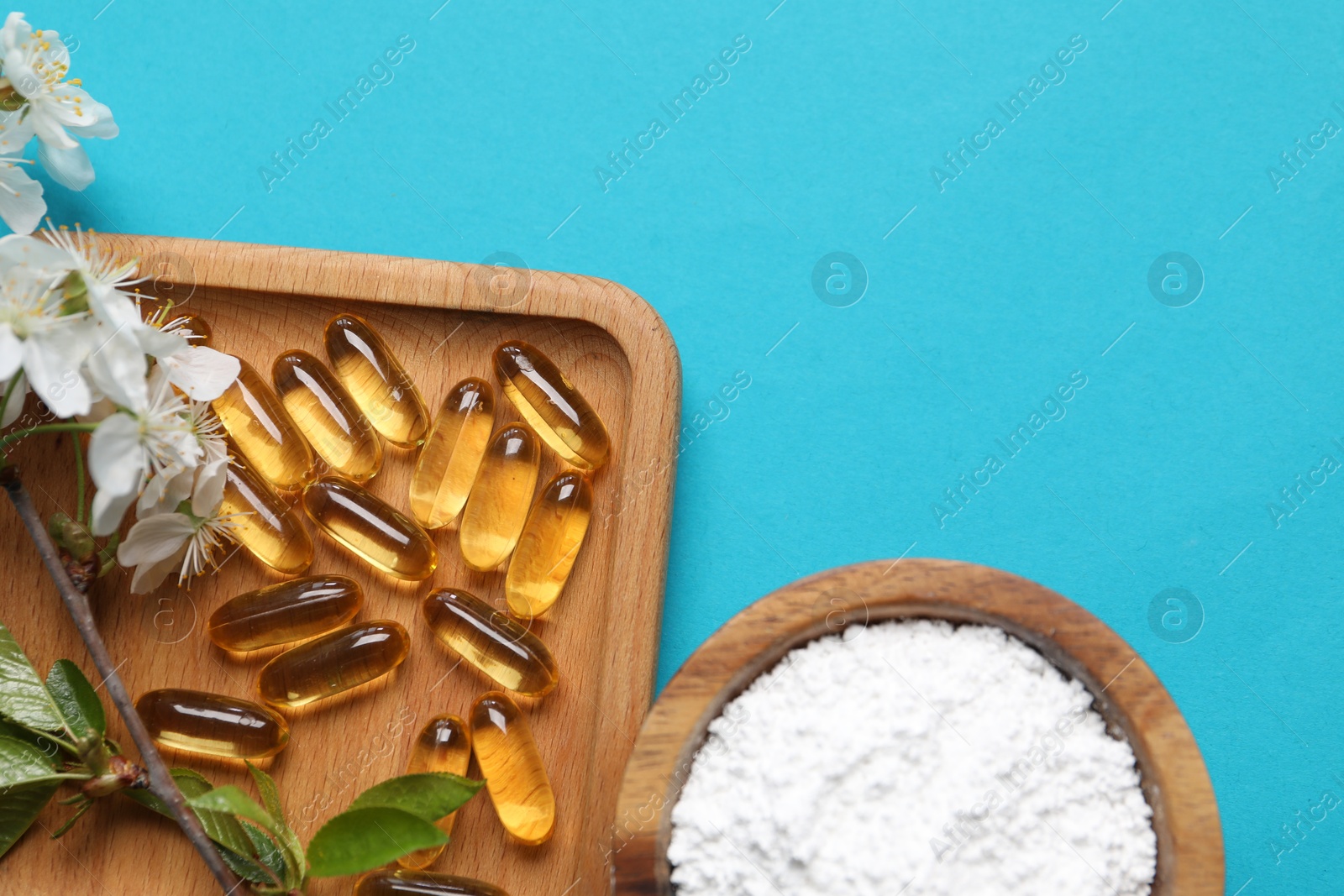 Collagen capsules, powder and blossoms on light blue background, flat lay. Space for text Photo of Collagen capsules, powder and blossoms on light blue background, flat lay. Space for text