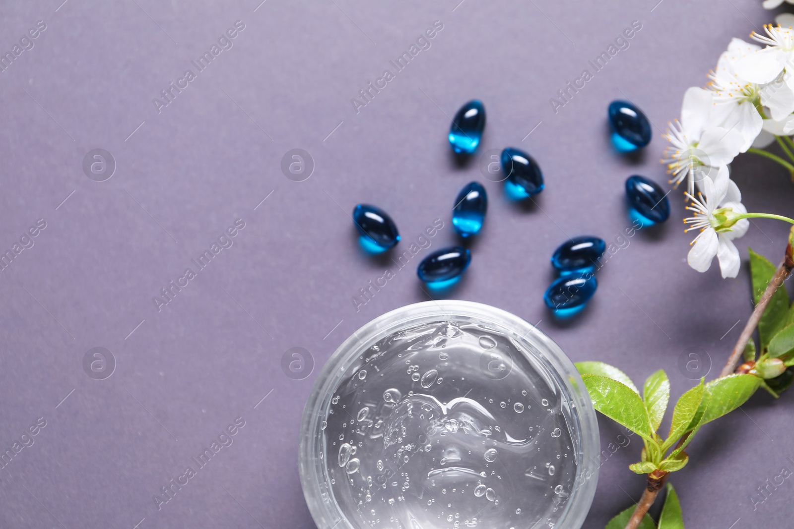 Collagen capsules, gel and blossoms on violet background, flat lay. Space for text Photo of Collagen capsules, gel and blossoms on violet background, flat lay. Space for text