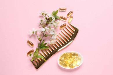 Photo of Collagen capsules, blossoms and comb on pink background, flat lay