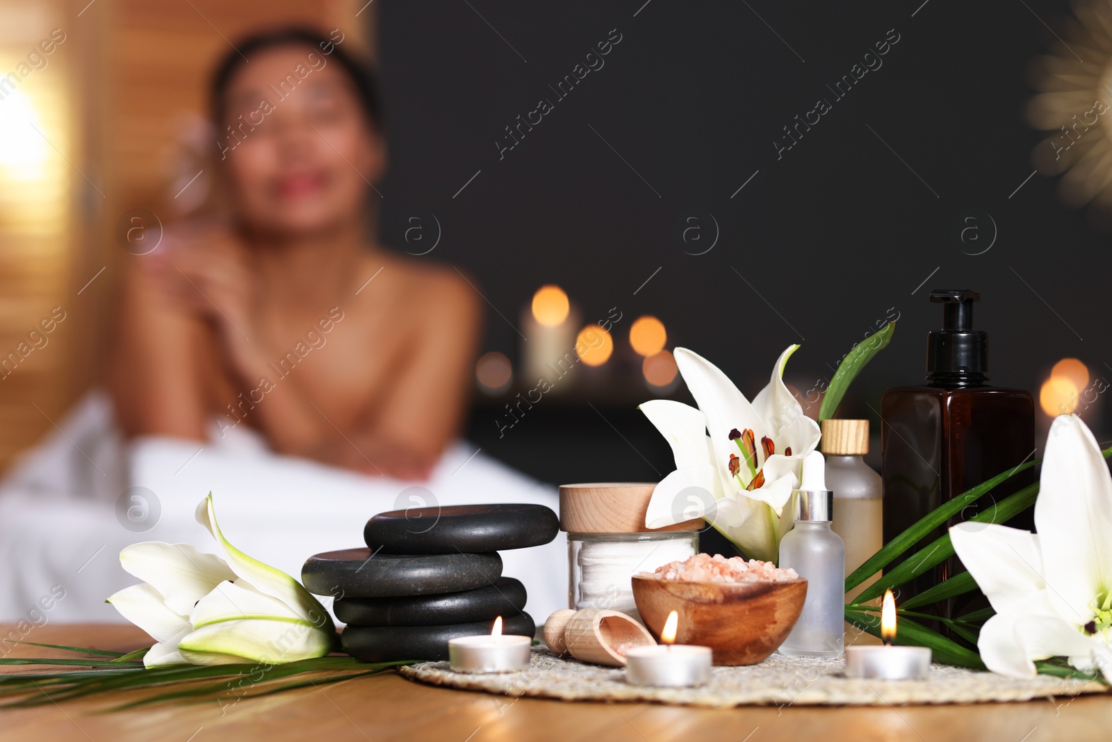 Beautiful woman relaxing on massage couch indoors, focus on different spa products and lily flowers Photo of Beautiful woman relaxing on massage couch indoors, focus on different spa products and lily flowers