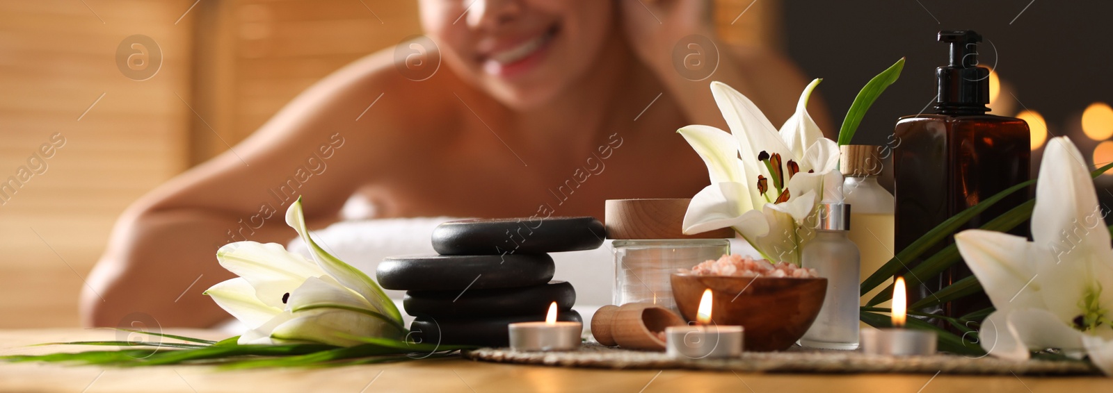 Beautiful woman relaxing on massage couch indoors, focus on different spa products and lily flowers Photo of Beautiful woman relaxing on massage couch indoors, focus on different spa products and lily flowers